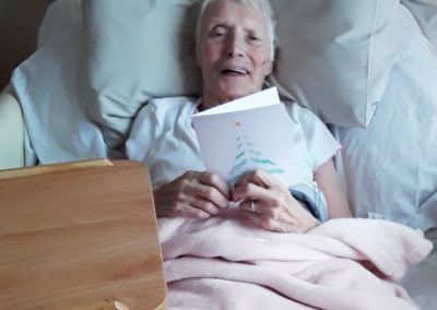 A lady resident smiling in bed holding a Christmas card